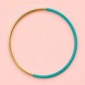Green dip enamel stacking bangle with a polished gold tone finish on a pale pink background.