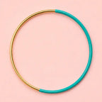 Green dip enamel stacking bangle with a polished gold tone finish on a pale pink background.