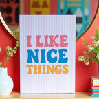 Colourful I Like Nice Things A5 print with bold pink, blue and yellow lettering, styled against a vibrant red wall.