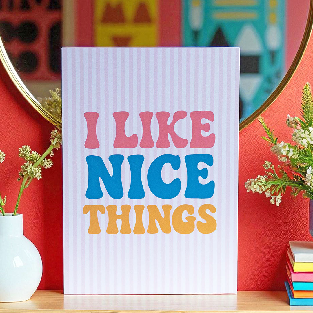 Colourful I Like Nice Things A5 print with bold pink, blue and yellow lettering, styled against a vibrant red wall.