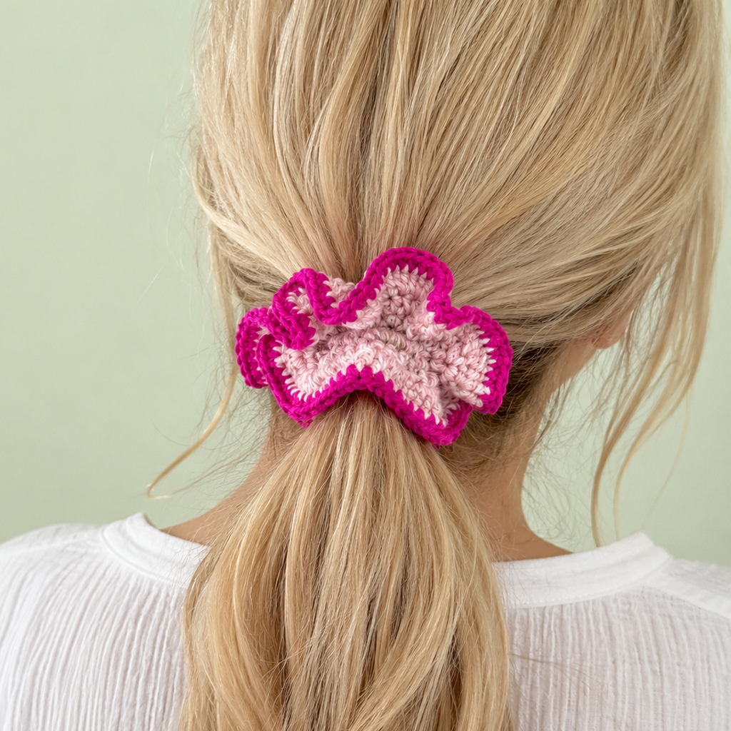 Blush pink and raspberry crochet scrunchie handmade by Corrine worn around a blonde ponytail.