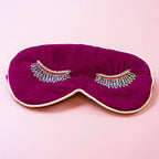 Magenta velvet eye mask with sparkling beaded eyelash detail and pale gold edging on a pink background.