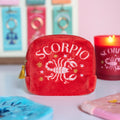 Red velvet Scorpio embroidered zodiac pouch displayed with colourful accessories and matching Scorpio candle.