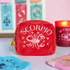 Red velvet Scorpio embroidered zodiac pouch displayed with colourful accessories and matching Scorpio candle.