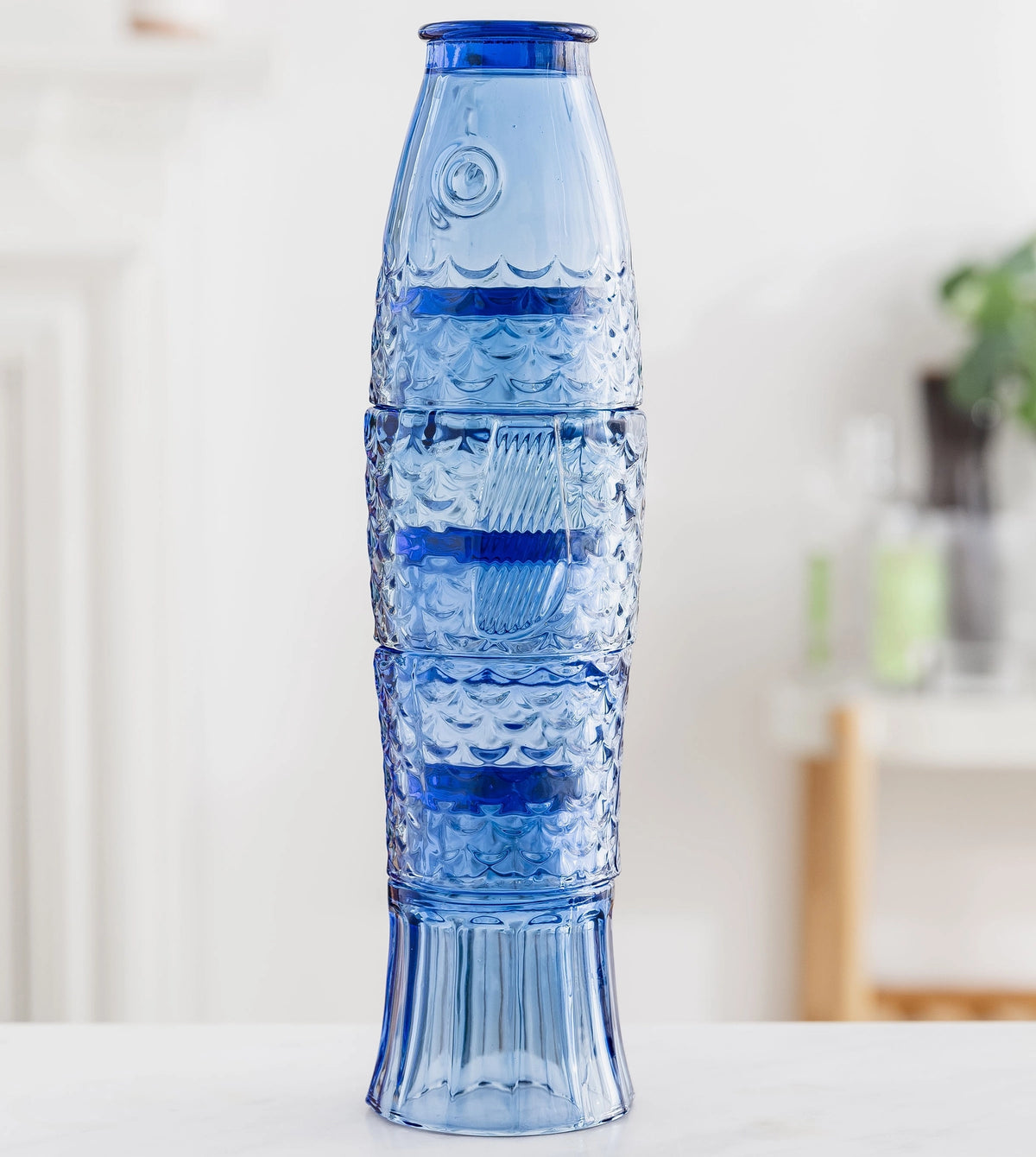 Four blue drinking glasses stacked together to create a tall fish shape.