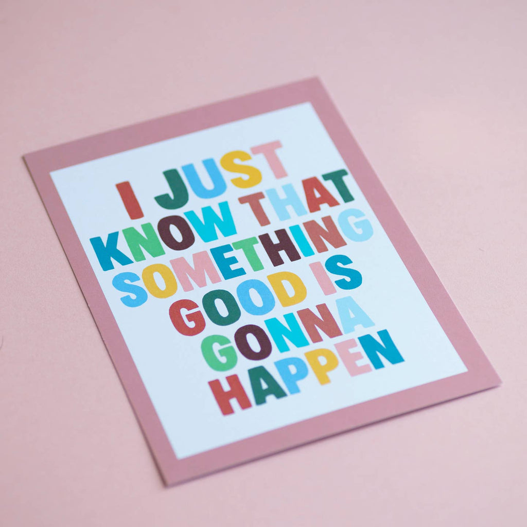 Joyful Something Good Is Gonna Happen A5 print with colourful typography and a soft pink border, photographed at an angle.