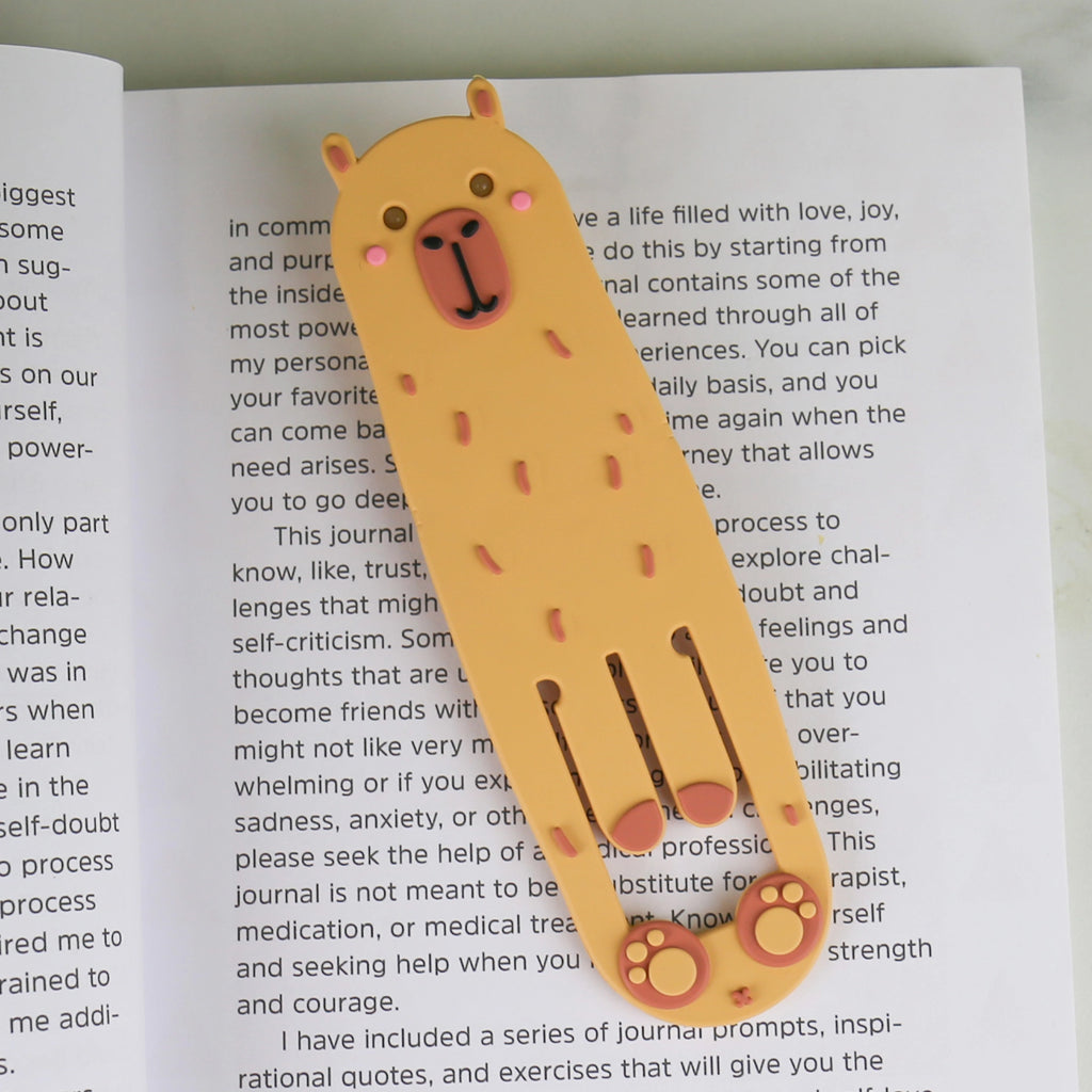 Cute orange capybara reading light and bookmark resting inside an open book.