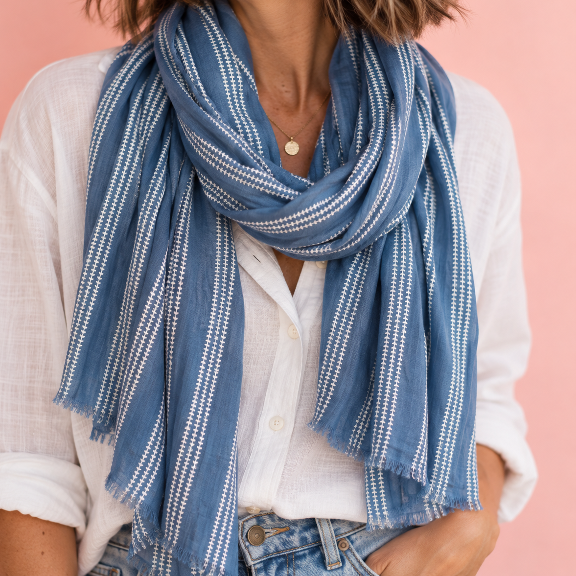 Woman wearing a soft blue scarf with white textured stripes, styled with a white shirt and jeans.