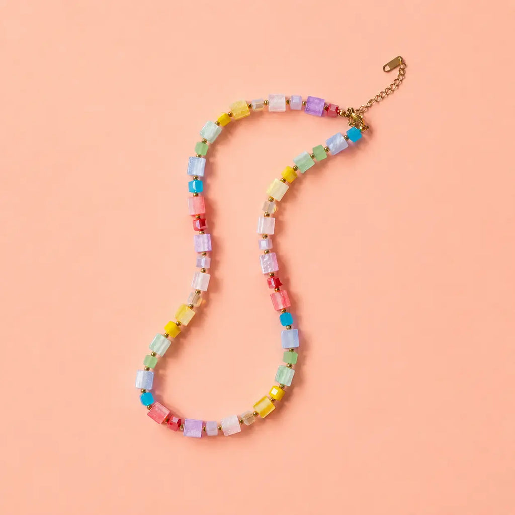 Colourful pastel crystal cube bead necklace with gold plated extension chain on a peach background.