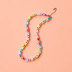 Colourful pastel crystal cube bead necklace with gold plated extension chain on a peach background.