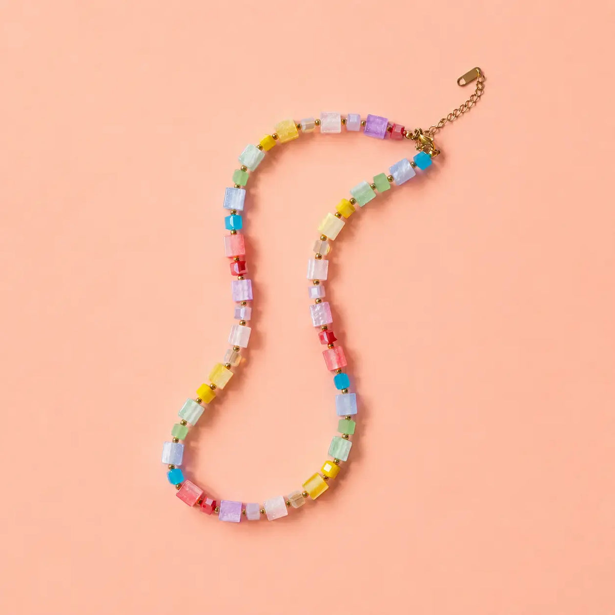 Colourful pastel crystal cube bead necklace with gold plated extension chain on a peach background.