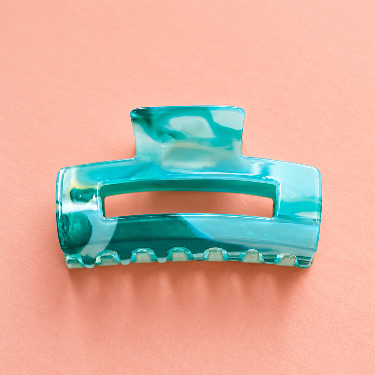 Translucent aqua and turquoise marble effect acrylic claw hair clip on a soft peach background.