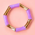 Lilac acrylic and gold bamboo inspired stretch bracelet on a pale pink background.