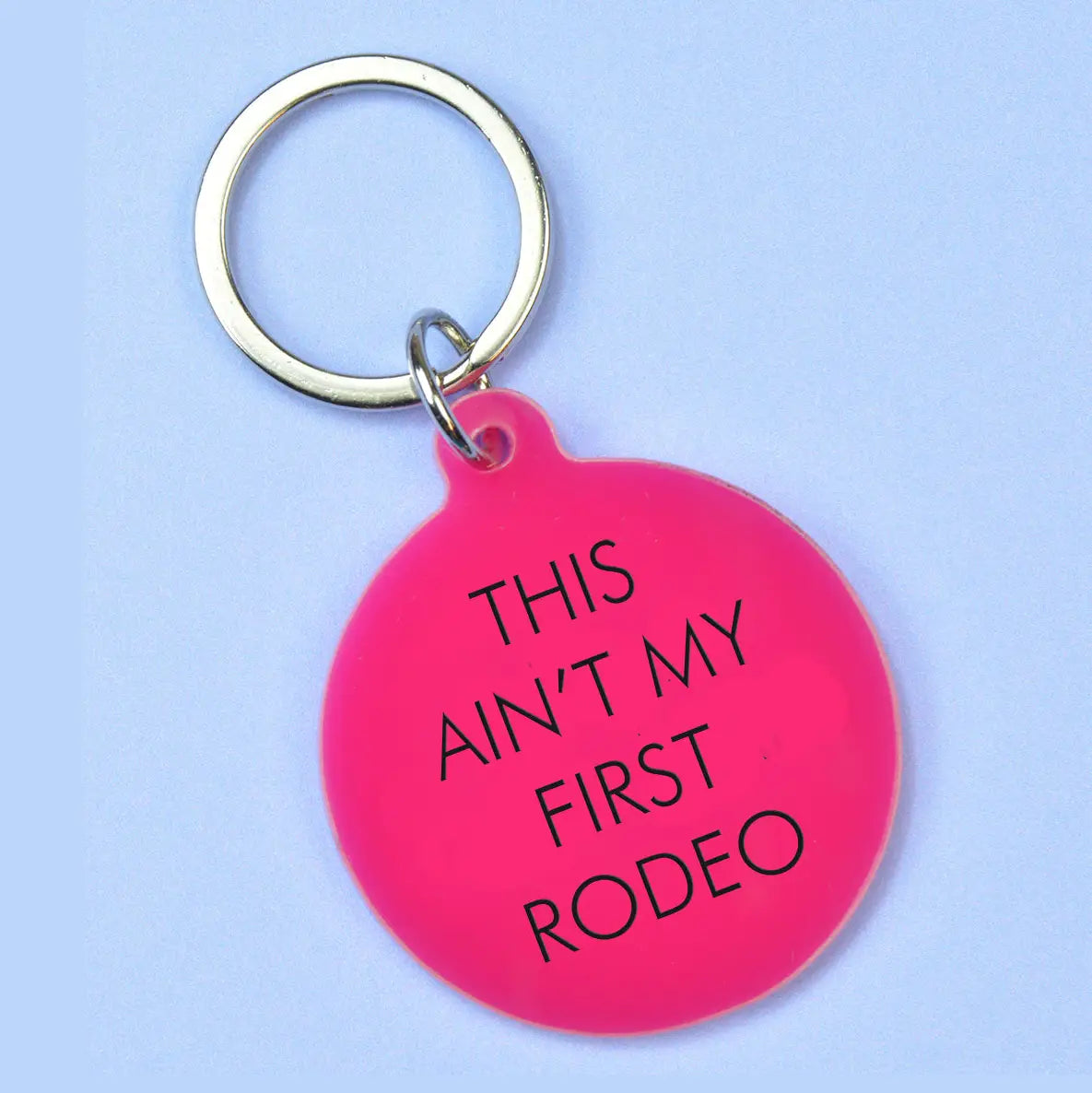 Hot pink round keyring with black This Ain't My First Rodeo lettering and silver-tone metal keyring attachment.