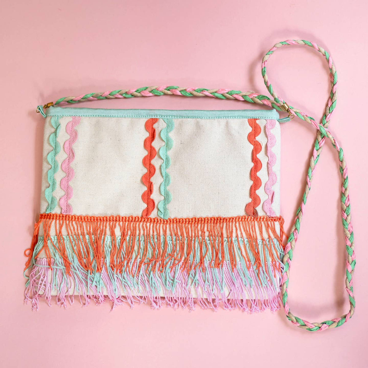 Playful canvas crossbody bag with mint, coral and pink ric rac, swishy layered fringe and a colourful braided strap on a pink background.