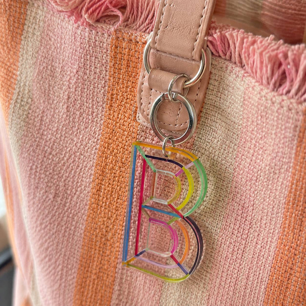Colourful letter B acrylic bag charm attached to a pink striped handbag with a silver-tone keyring.