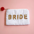 White velvet zip pouch with sparkling gold ‘BRIDE’ lettering and bright red pom pom zip pull.