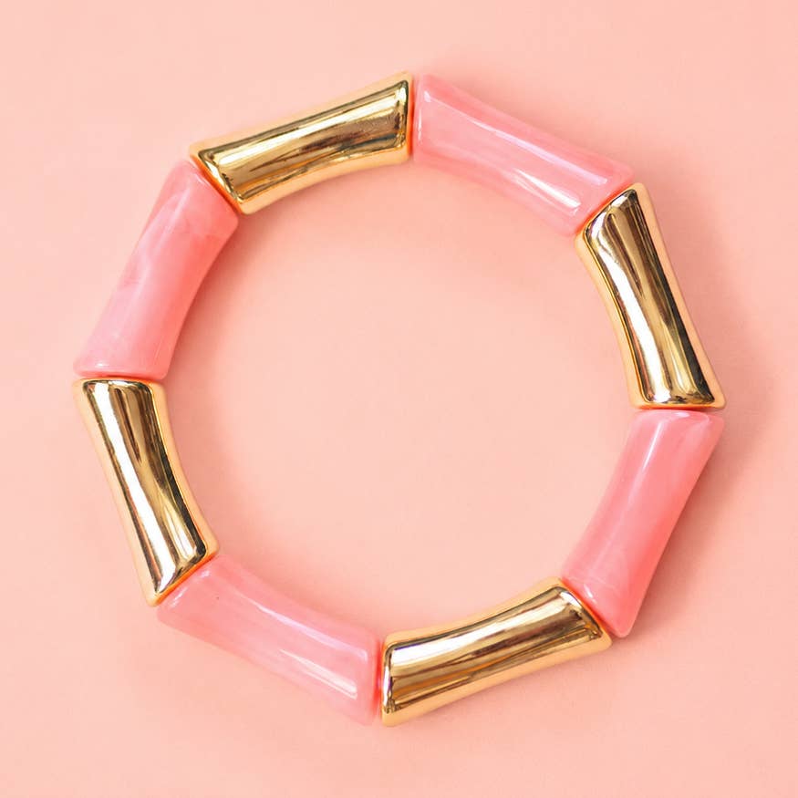 Coral acrylic and gold bamboo inspired stretch bracelet on a pale pink background.
