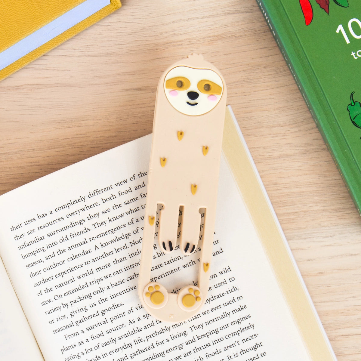 Flexible sloth reading light and bookmark resting inside an open book.