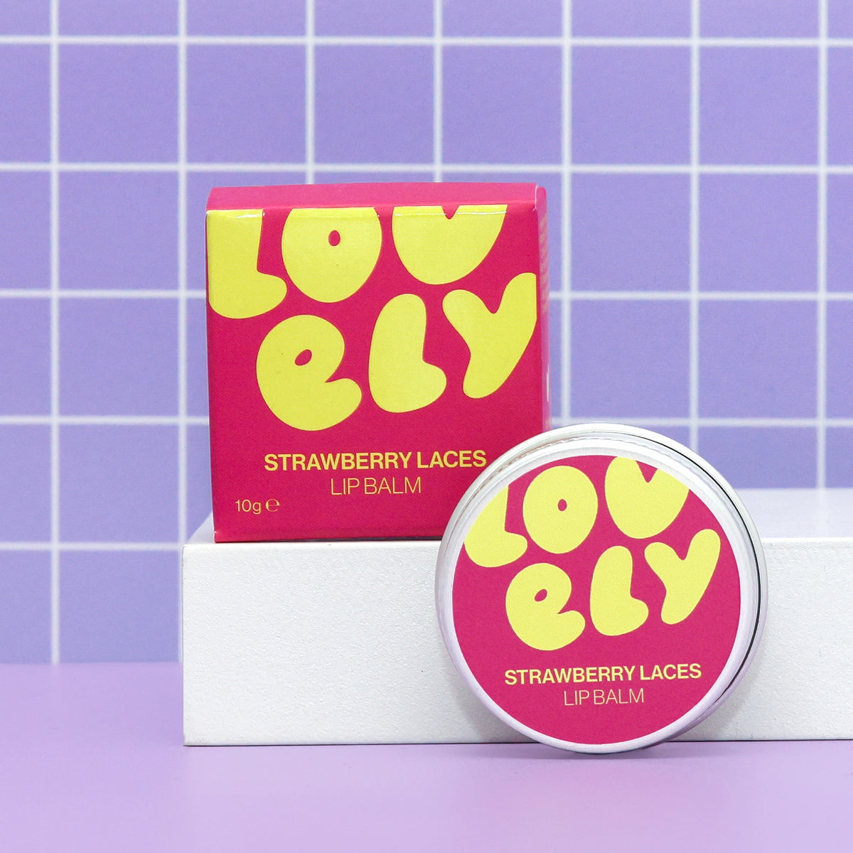 Strawberry Laces Lip Balm tin and colourful box displayed against a lilac tiled background.
