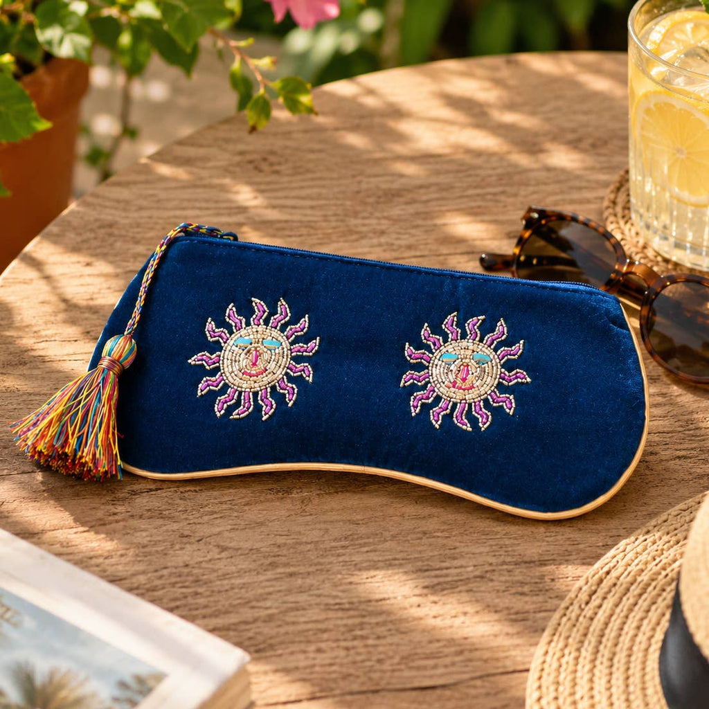 Navy velvet beaded sun glasses pouch with colourful tassel displayed beside sunglasses on a wooden table.