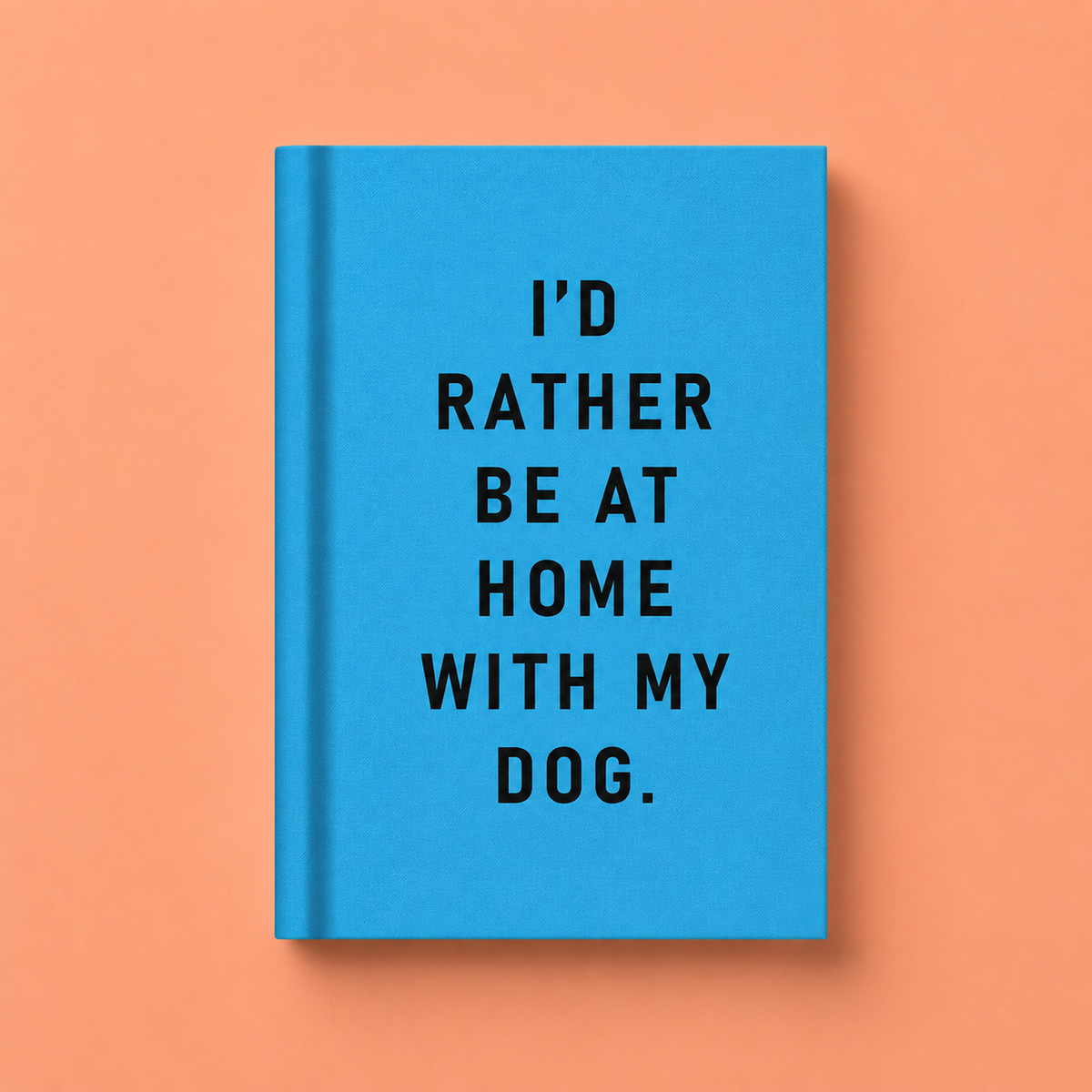 Bright blue A7 fabric hardback notebook with black I’d Rather Be At Home With My Dog text on a peach background.