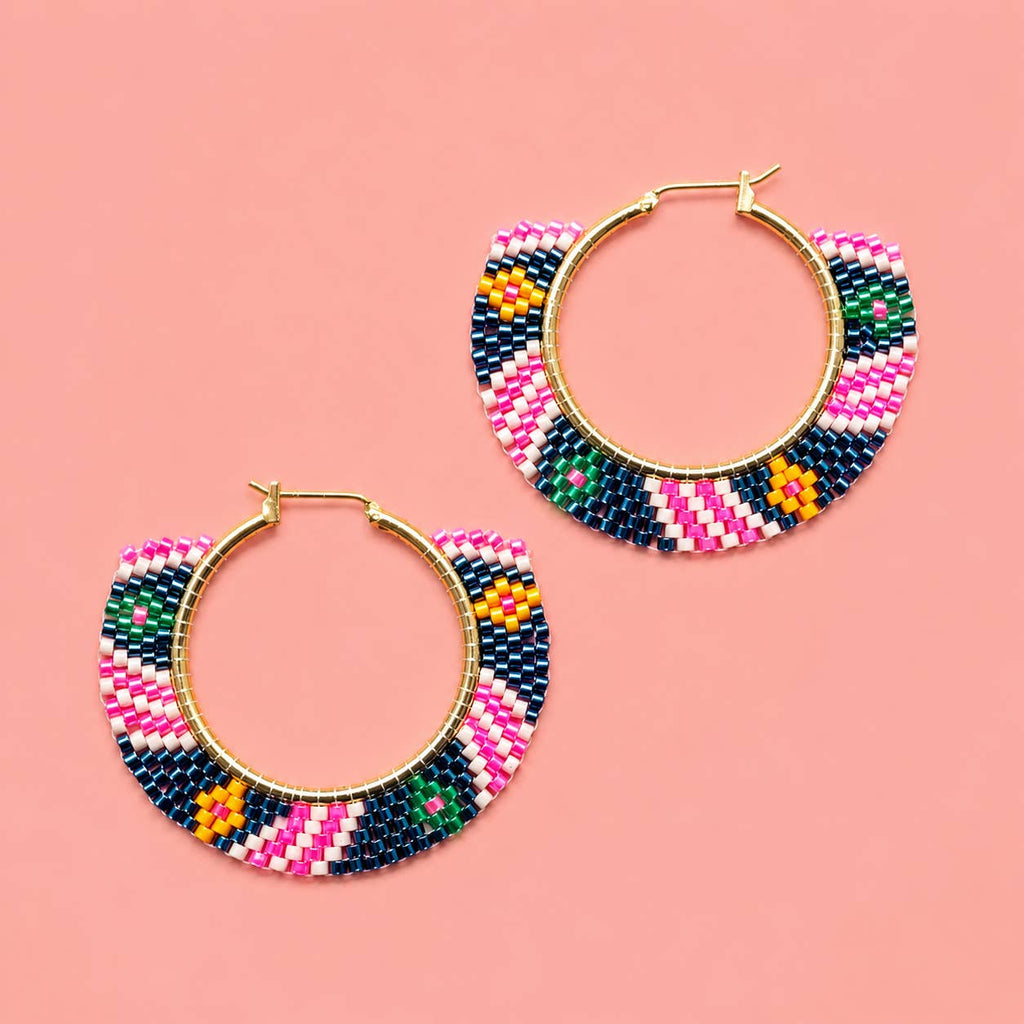 Pair of pink and navy geometric beaded hoop earrings with gold coloured hoops on a pink background.