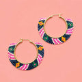 Pair of pink and navy geometric beaded hoop earrings with gold coloured hoops on a pink background.