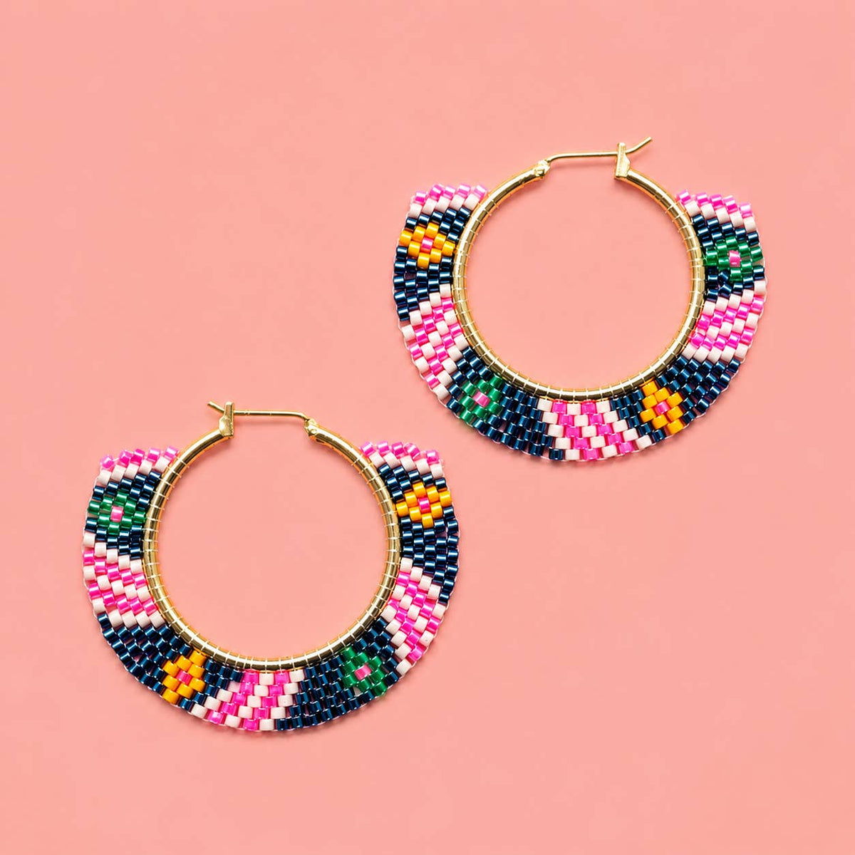 Pair of pink and navy geometric beaded hoop earrings with gold coloured hoops on a pink background.