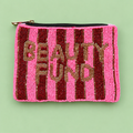 A rectangular beaded pouch with pink and dark red vertical stripes, featuring the words 'BEAUTY FUND' in gold beaded letters. The pouch has a black zipper with a gold pull tab and is photographed flat on a light green background.