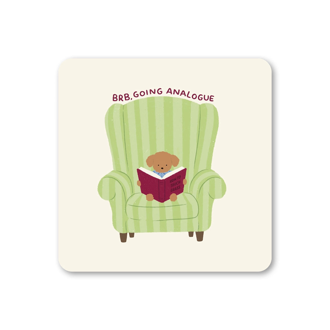 Cream square coaster featuring a small dog reading a book in a green striped armchair with BRB Going Analogue above.