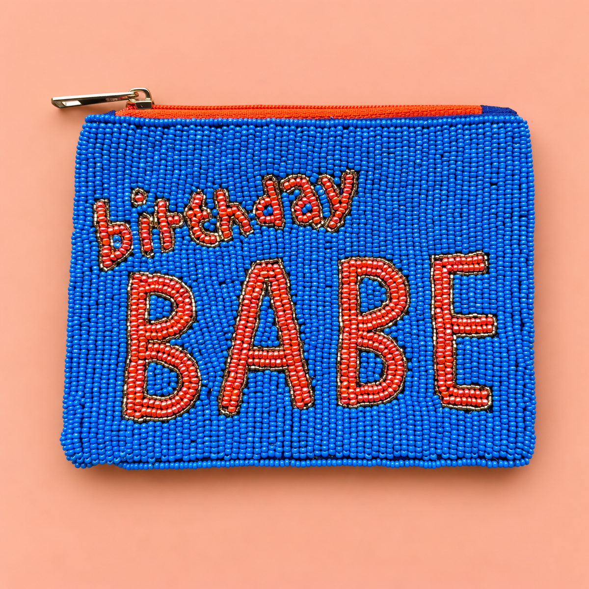 Electric blue beaded pouch with bold orange Birthday Babe lettering, contrasting orange zip and gold zip pull on a peach background.