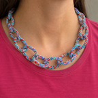 Chunky blue mix beaded statement chain necklace worn with a pink top, showing its colourful oversized interlocking links.