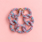 Chunky blue mix beaded statement chain bracelet with oversized multicoloured interlocking links and gold tone detail on a soft pink background.
