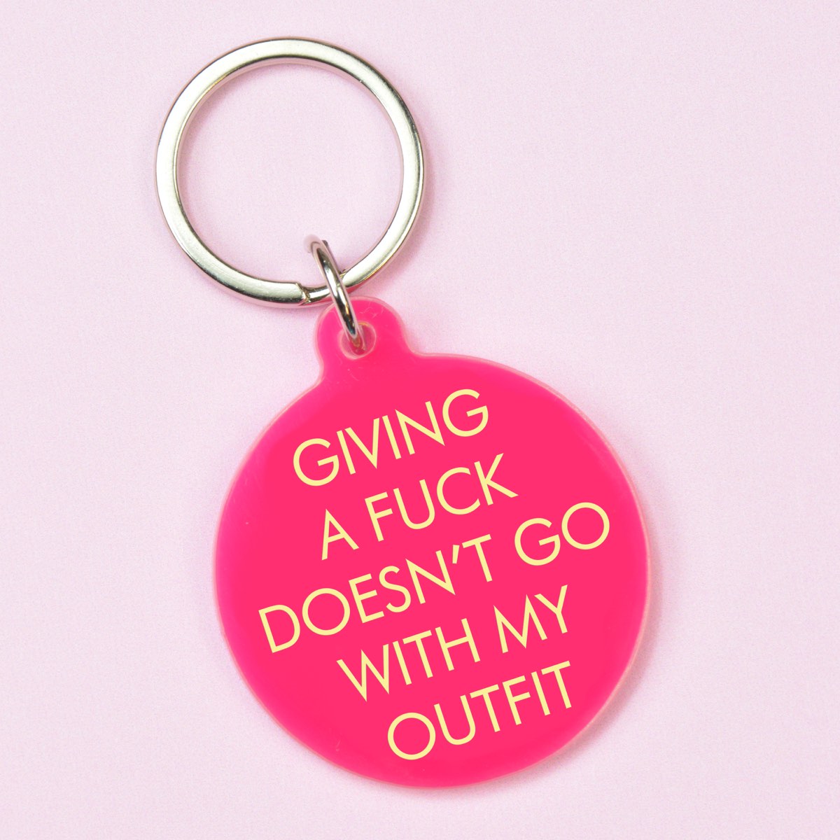 Hot pink round keyring with pale yellow Giving a Fuck Doesn't Go With My Outfit lettering and silver-tone keyring.