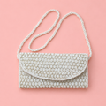 White beaded shoulder and clutch bag with intricate metallic detailing and long beaded strap on a soft pink backgro