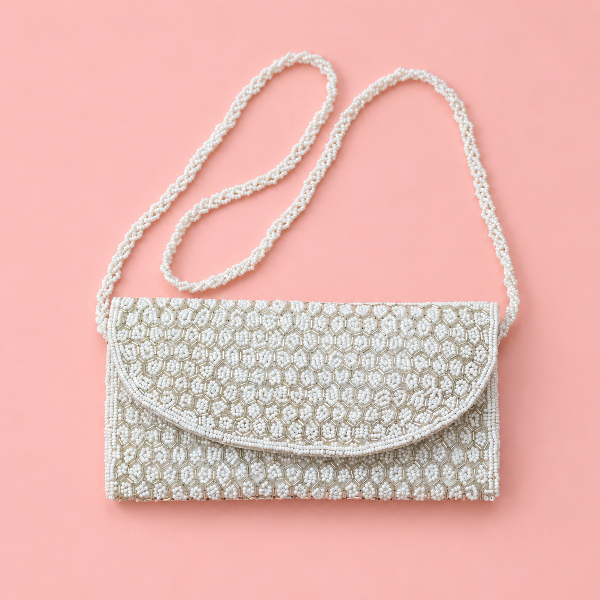 White beaded shoulder and clutch bag with intricate metallic detailing and long beaded strap on a soft pink backgro