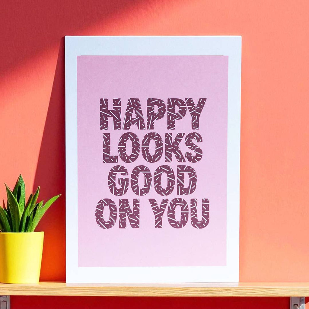Happy Looks Good On You A5 art print with bold burgundy patterned lettering on a joyful soft pink background.