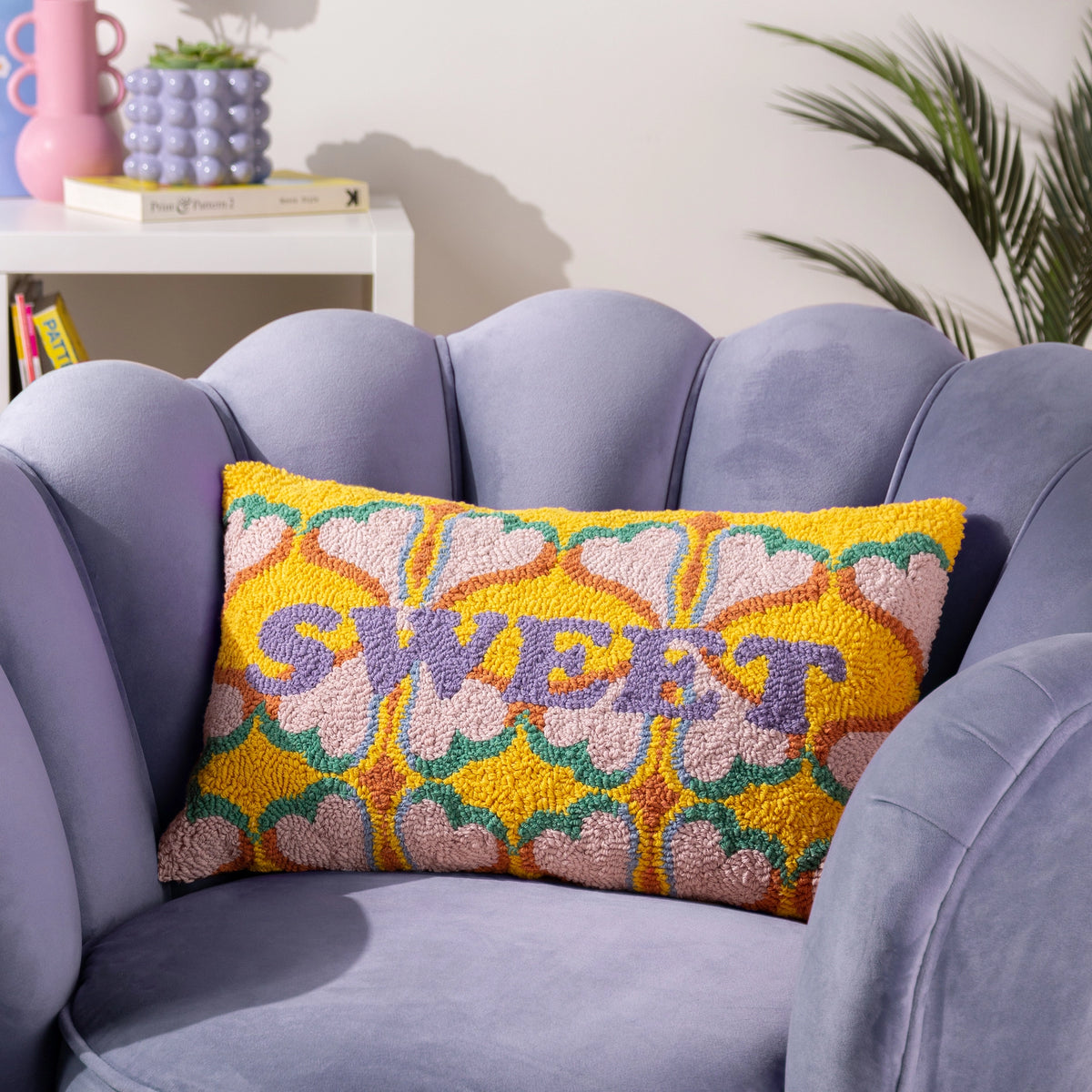 Colourful SWEET cushion with pink hearts and lilac lettering styled on a soft lilac armchair.