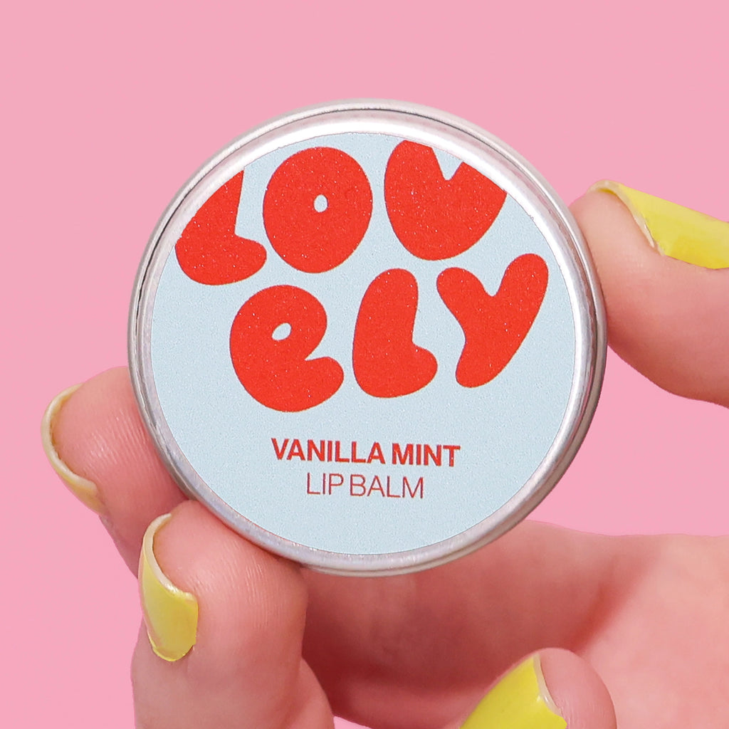 Vanilla Mint Lip Balm 10g tin held in a hand against a pink background.