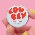 Vanilla Mint Lip Balm 10g tin held in a hand against a pink background.