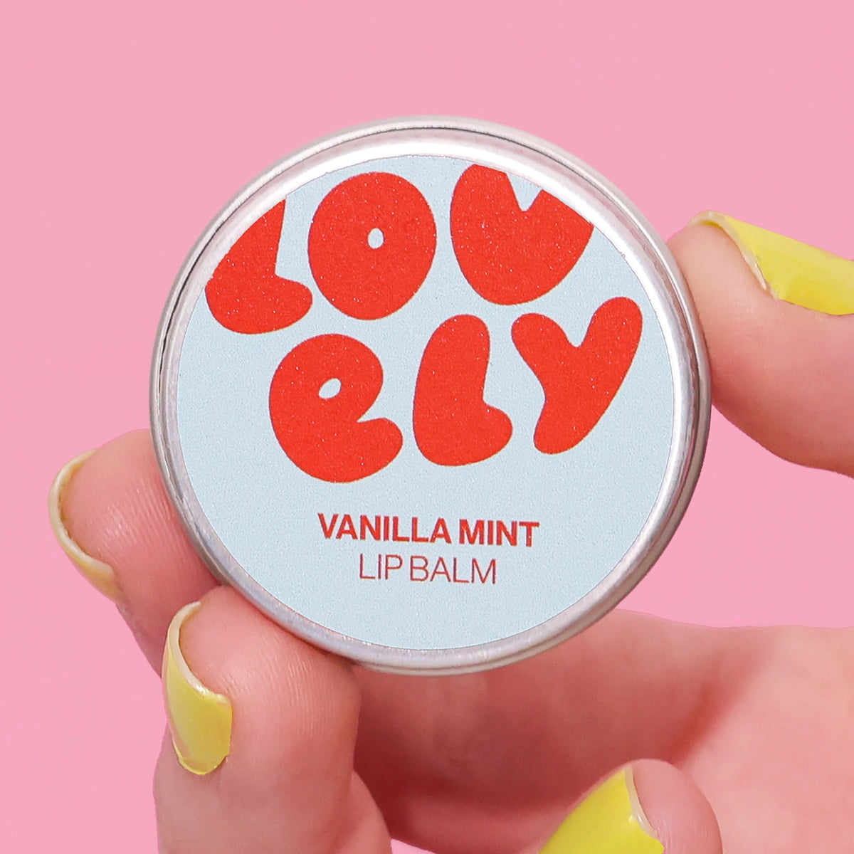 Vanilla Mint Lip Balm 10g tin held in a hand against a pink background.