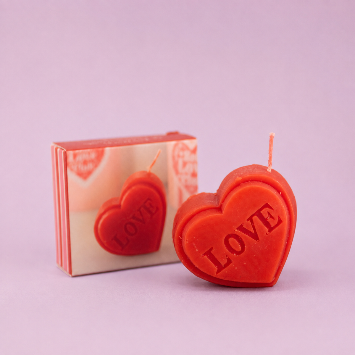 Mini red heart shaped candle with LOVE lettering displayed beside its matching gift box on a soft lilac background.