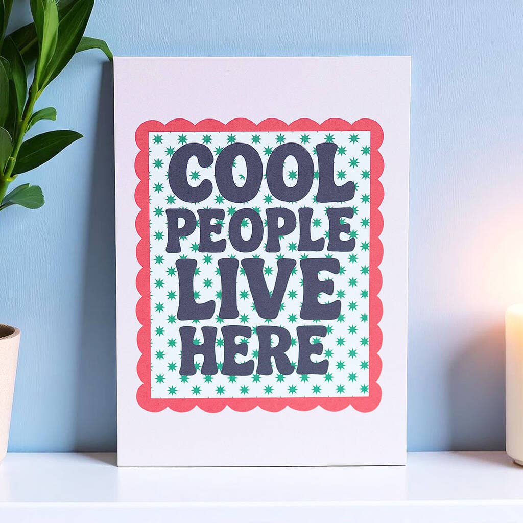 Cheerful Cool People Live Here A5 art print with bold retro lettering, green starbursts and a red scalloped border displayed on a shelf.