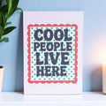 Cheerful Cool People Live Here A5 art print with bold retro lettering, green starbursts and a red scalloped border displayed on a shelf.