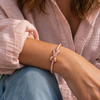 Pale pink enamel bow bangle with gold-tone detailing styled on the wrist with a pink blouse and denim.