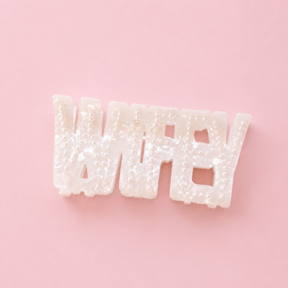 Pearlescent white WIFEY claw hair clip decorated with small pearl details on a soft pink background.