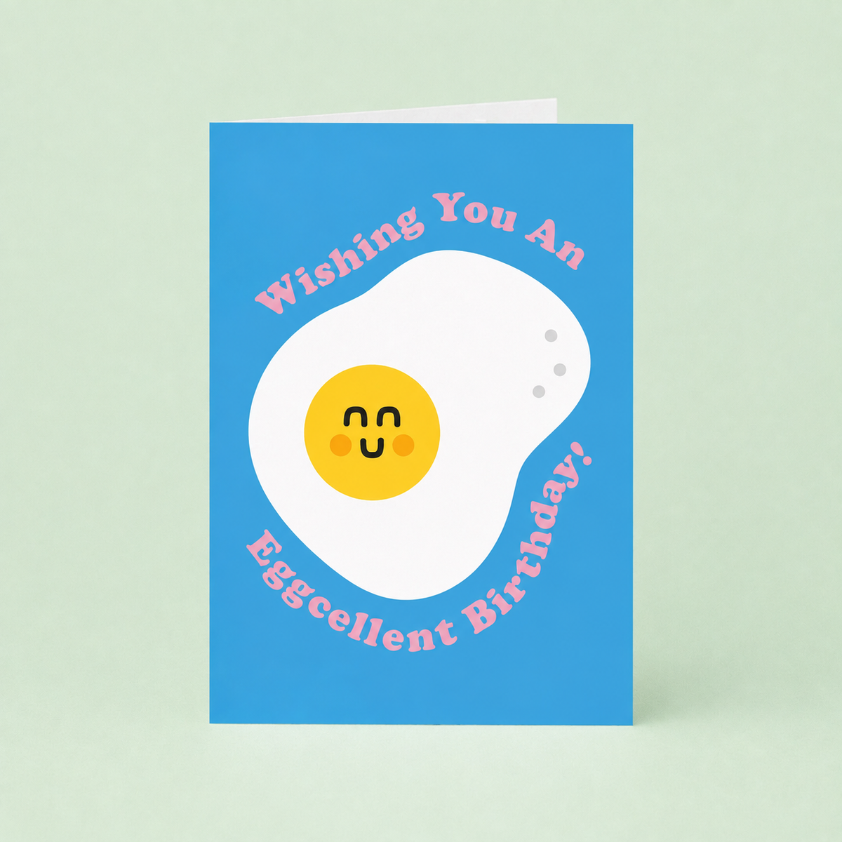 Bright blue birthday card featuring a smiling fried egg and pink Wishing You An Eggcellent Birthday lettering.