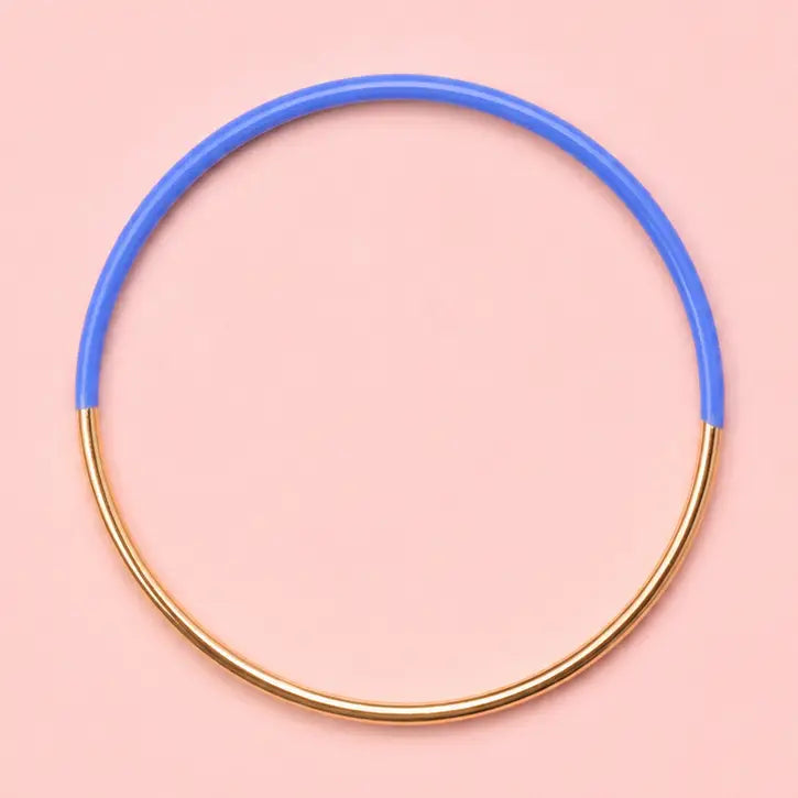 Blue dip enamel stacking bangle with a polished gold tone finish on a pale pink background.