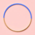 Blue dip enamel stacking bangle with a polished gold tone finish on a pale pink background.